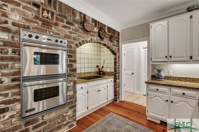 kitchen featuring stainless steel double oven, white cabinetry, light hardwood / wood-style flooring, and dark stone counters