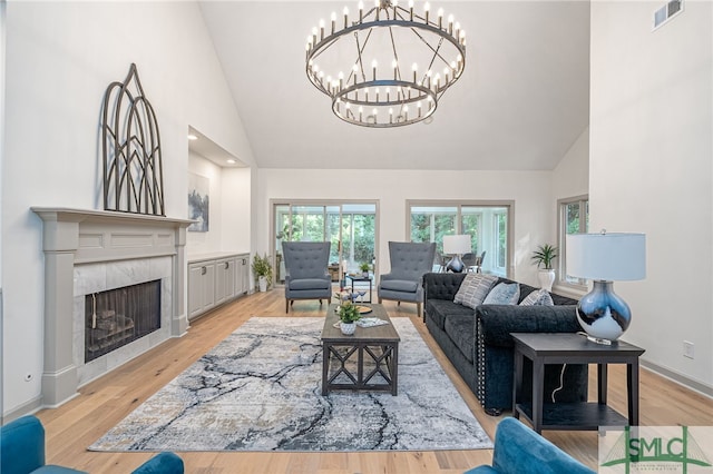 living room with a tile fireplace, light wood-type flooring, a chandelier, and high vaulted ceiling