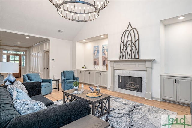 living room with sink, light hardwood / wood-style flooring, high vaulted ceiling, a chandelier, and a fireplace