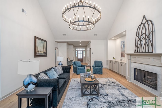 living room with high vaulted ceiling, a chandelier, a tile fireplace, and light hardwood / wood-style flooring