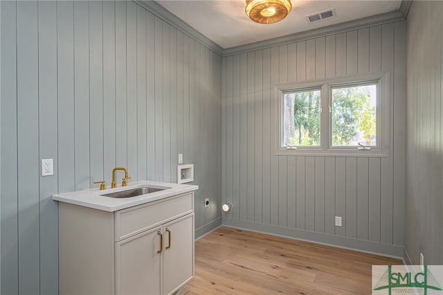 clothes washing area featuring sink, wooden walls, hookup for a washing machine, light hardwood / wood-style flooring, and ornamental molding