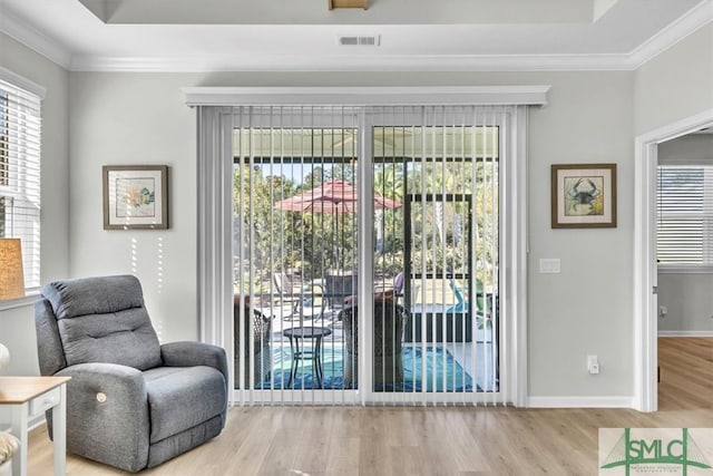 living area with ornamental molding, light wood-type flooring, and a raised ceiling