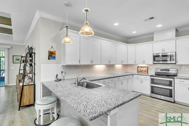 kitchen with sink, appliances with stainless steel finishes, kitchen peninsula, and white cabinetry