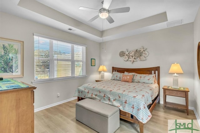 bedroom with ceiling fan, a tray ceiling, and light wood-type flooring