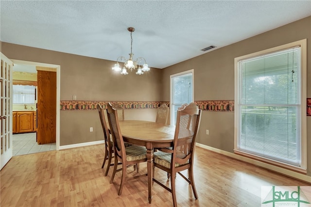 dining room with an inviting chandelier, sink, a textured ceiling, and light wood-type flooring