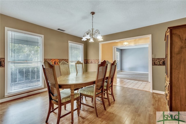 dining room with a textured ceiling, an inviting chandelier, and light wood-type flooring