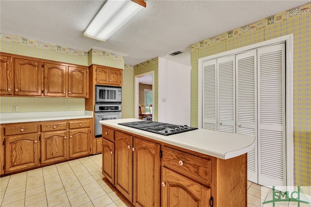 kitchen with light tile patterned floors, a textured ceiling, appliances with stainless steel finishes, and a center island