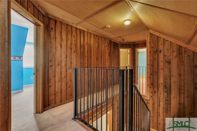 corridor featuring lofted ceiling, wooden walls, and light carpet