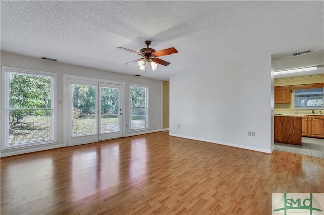 unfurnished living room featuring light hardwood / wood-style floors, a textured ceiling, plenty of natural light, and ceiling fan