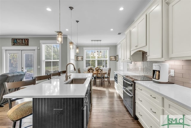 kitchen with stainless steel electric stove, white cabinets, a kitchen island with sink, decorative light fixtures, and sink