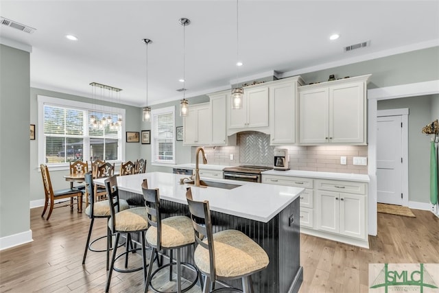 kitchen with backsplash, an island with sink, white cabinetry, light hardwood / wood-style flooring, and decorative light fixtures