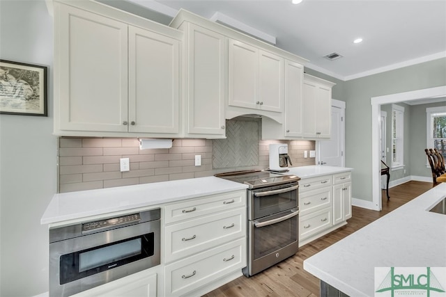 kitchen with light hardwood / wood-style floors, appliances with stainless steel finishes, backsplash, and white cabinets