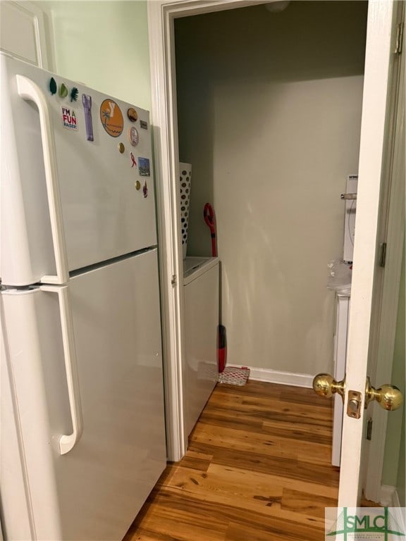 kitchen featuring washer / dryer, white cabinets, hardwood / wood-style flooring, and stainless steel refrigerator