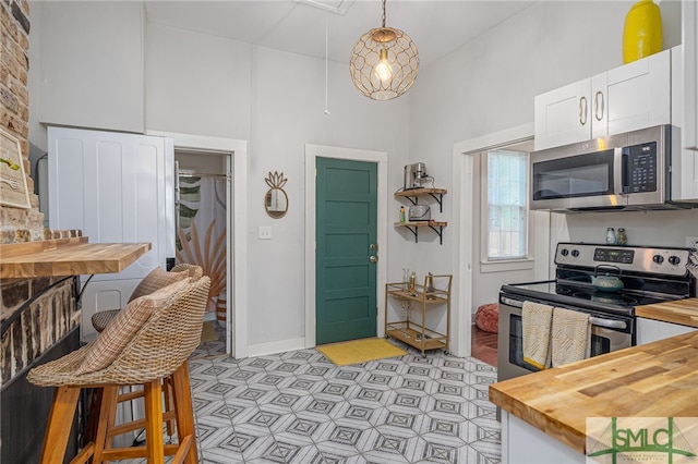 kitchen with appliances with stainless steel finishes, white cabinets, a high ceiling, hanging light fixtures, and butcher block counters