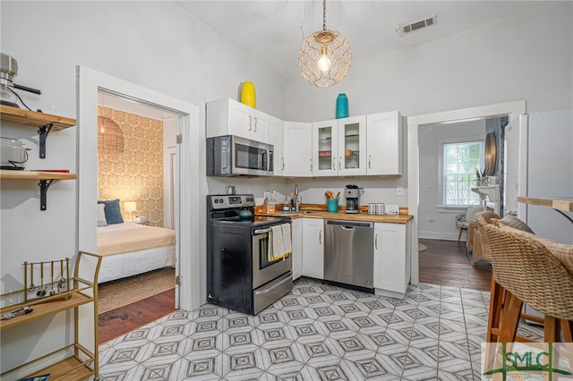 kitchen featuring hanging light fixtures, appliances with stainless steel finishes, butcher block countertops, light hardwood / wood-style floors, and white cabinetry