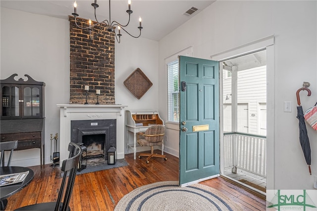 foyer entrance featuring wood-type flooring, a fireplace, and an inviting chandelier