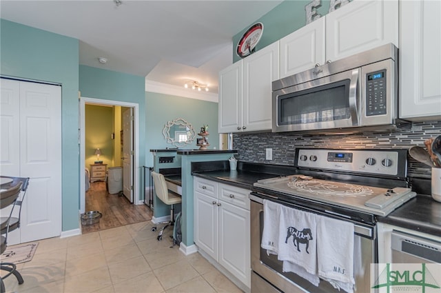 kitchen with white cabinets, dark countertops, stainless steel appliances, and backsplash