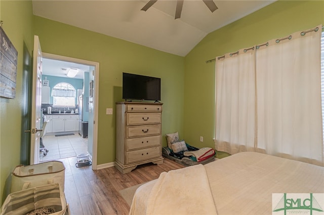 bedroom with light wood-style flooring, ensuite bathroom, a ceiling fan, vaulted ceiling, and a sink