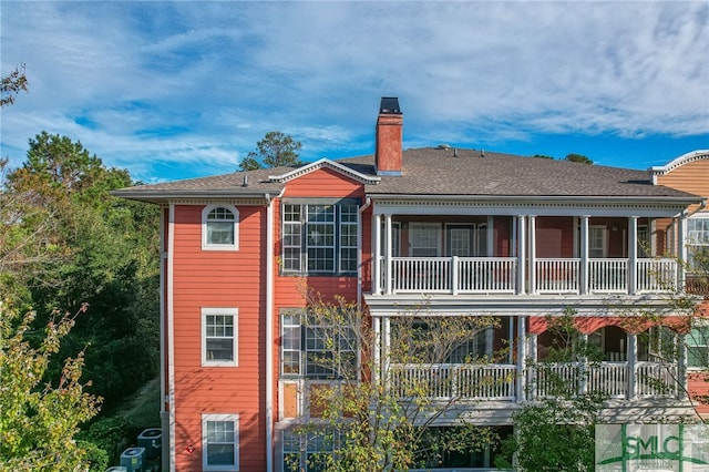 back of property featuring roof with shingles, a chimney, and a balcony