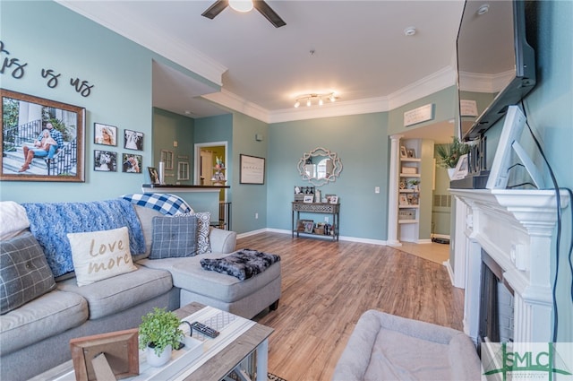 living area with a fireplace, ornamental molding, a ceiling fan, wood finished floors, and baseboards