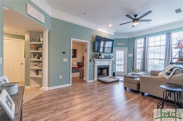 living area featuring decorative columns, a fireplace, visible vents, light wood-style flooring, and ornamental molding