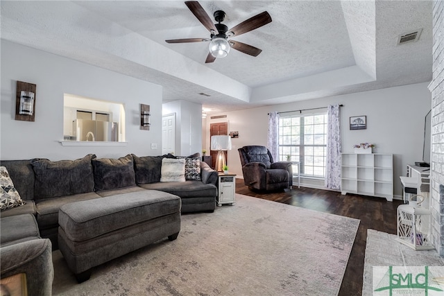 living room featuring a textured ceiling, ceiling fan, dark wood-type flooring, and a raised ceiling