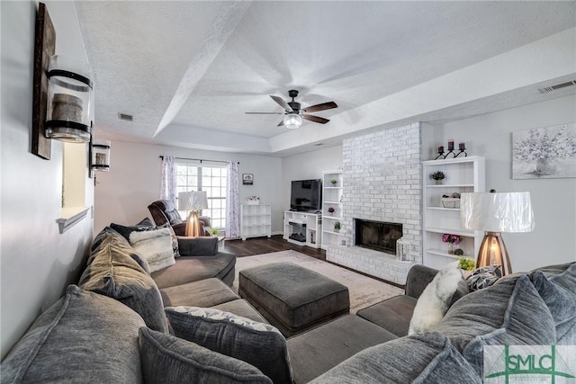 living room with a textured ceiling, ceiling fan, a raised ceiling, hardwood / wood-style floors, and a fireplace