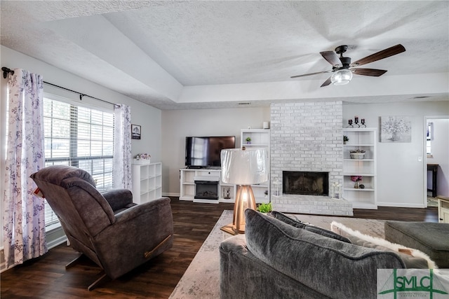 living room featuring dark hardwood / wood-style floors, ceiling fan, a tray ceiling, and a brick fireplace