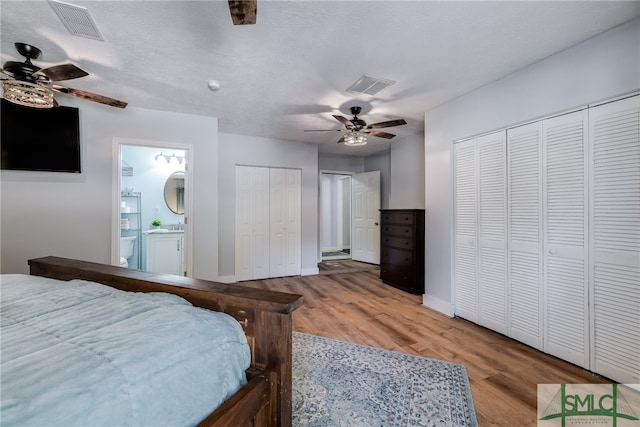 bedroom with light wood-type flooring, ensuite bathroom, two closets, a textured ceiling, and ceiling fan