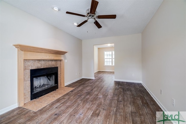 unfurnished living room with ceiling fan, a textured ceiling, a tile fireplace, and hardwood / wood-style floors