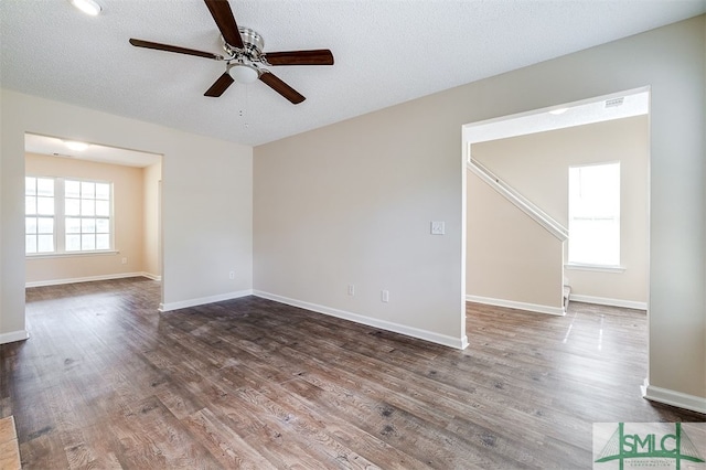 empty room featuring a textured ceiling, ceiling fan, dark hardwood / wood-style floors, and plenty of natural light