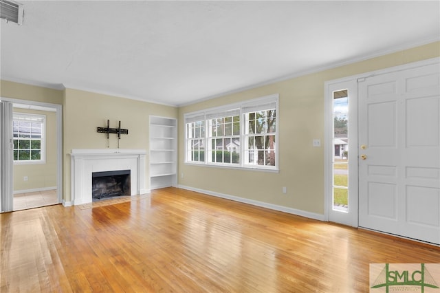 unfurnished living room featuring built in shelves, light hardwood / wood-style flooring, and a wealth of natural light