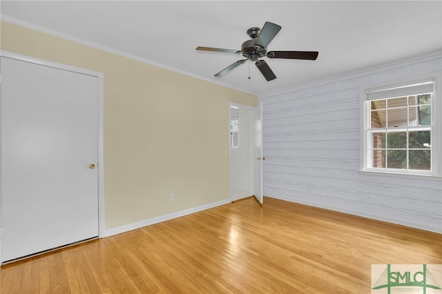 spare room with light hardwood / wood-style floors, ceiling fan, ornamental molding, and wood walls