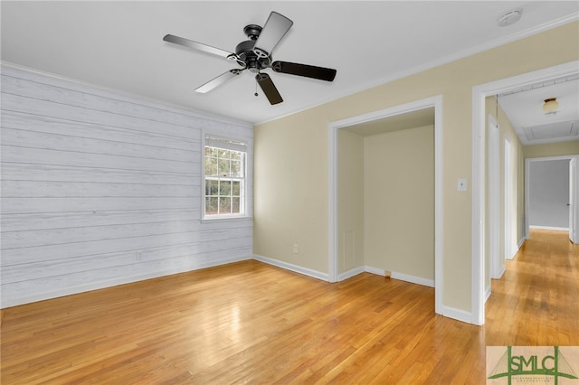 empty room with ceiling fan, light hardwood / wood-style flooring, wooden walls, and crown molding