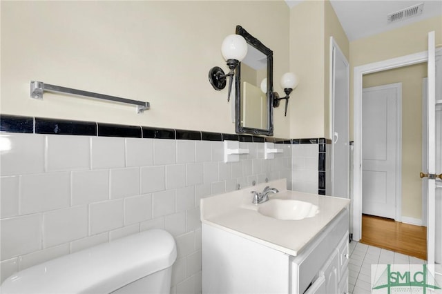 bathroom featuring toilet, tile patterned flooring, vanity, and tile walls