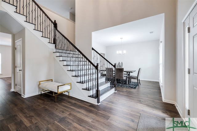 stairs with a towering ceiling, wood-type flooring, and a notable chandelier