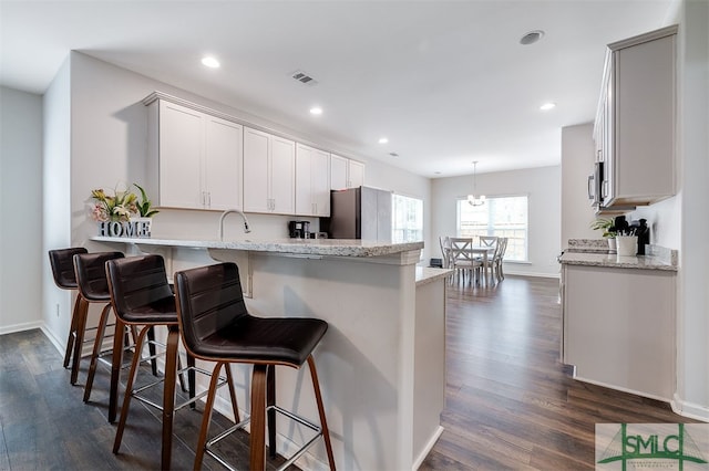 kitchen with white cabinetry, a breakfast bar, dark hardwood / wood-style floors, decorative light fixtures, and stainless steel fridge