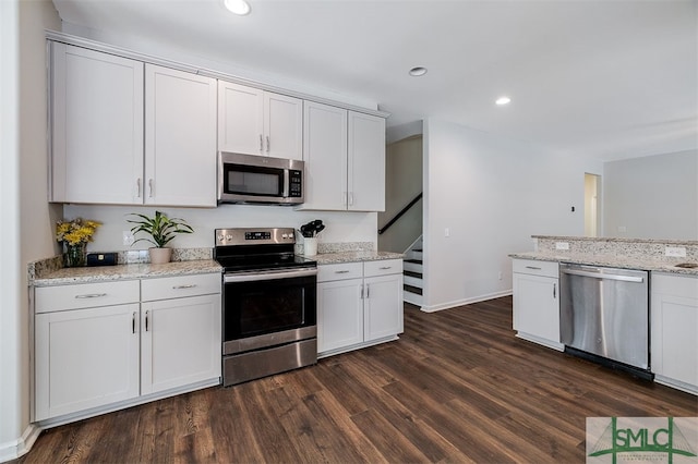 kitchen with white cabinets, stainless steel appliances, light stone counters, and dark hardwood / wood-style flooring