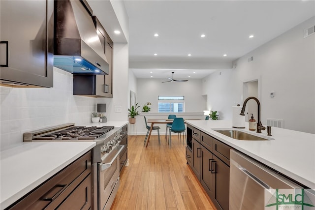 kitchen featuring appliances with stainless steel finishes, decorative backsplash, sink, wall chimney exhaust hood, and light hardwood / wood-style flooring