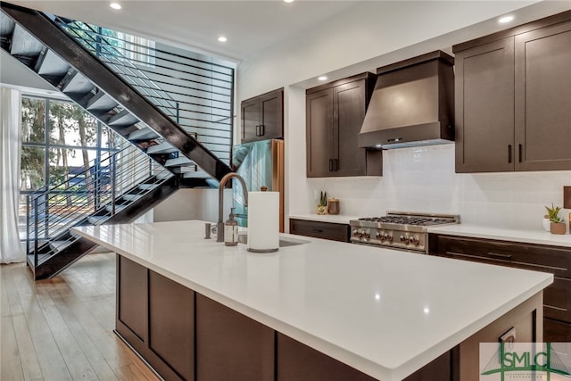 kitchen featuring sink, tasteful backsplash, light hardwood / wood-style flooring, wall chimney range hood, and high end range