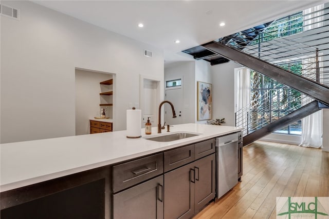 kitchen featuring dark brown cabinets, light wood-type flooring, stainless steel dishwasher, and sink