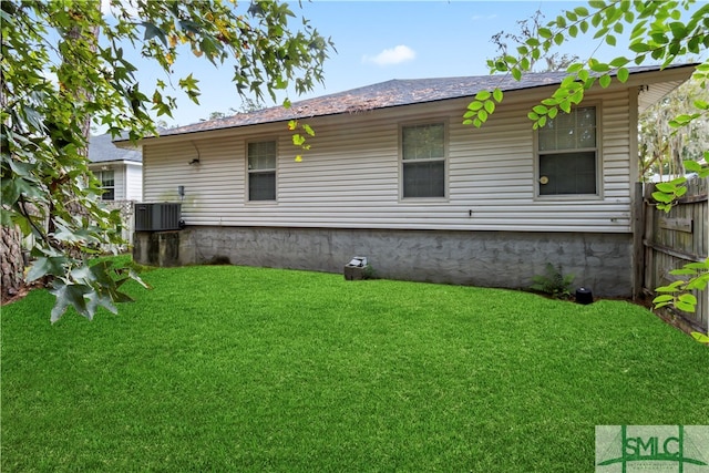 rear view of house with central AC unit and a yard