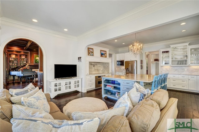 living room featuring dark wood-type flooring, a chandelier, sink, and ornamental molding