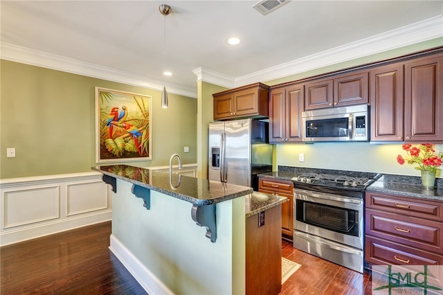 kitchen with a breakfast bar, appliances with stainless steel finishes, an island with sink, crown molding, and dark wood-type flooring