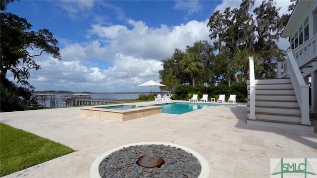 view of pool featuring a patio area, a water view, a fire pit, and an in ground hot tub