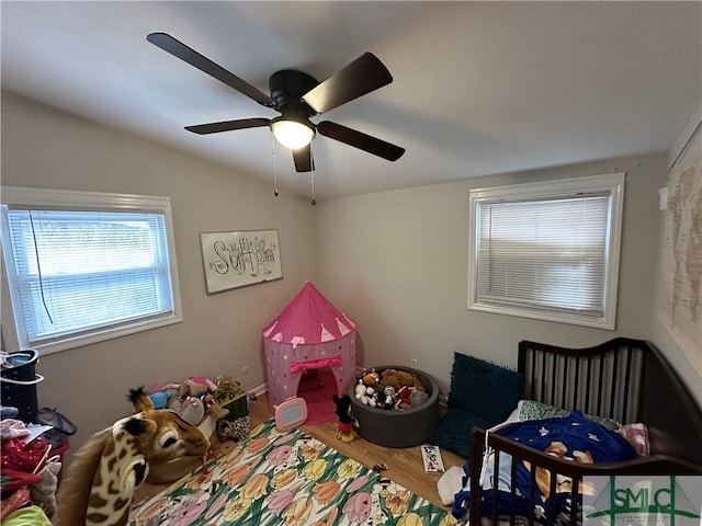 bedroom with ceiling fan, a crib, wood-type flooring, and vaulted ceiling