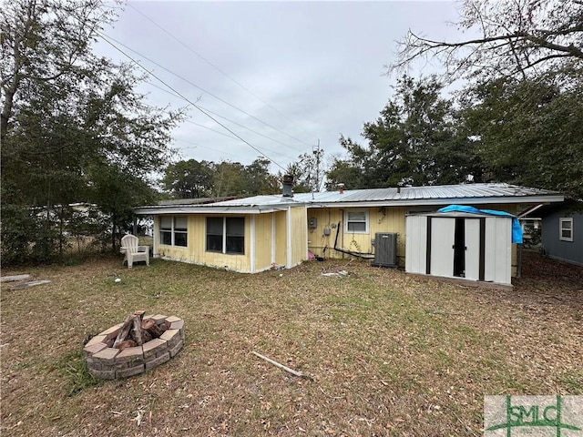 back of property featuring a fire pit, central AC unit, and a shed