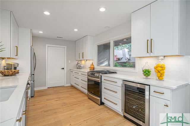 kitchen with white cabinets, appliances with stainless steel finishes, light hardwood / wood-style floors, and wine cooler