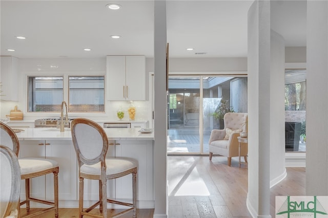 kitchen with white cabinetry, sink, a kitchen breakfast bar, backsplash, and light wood-type flooring