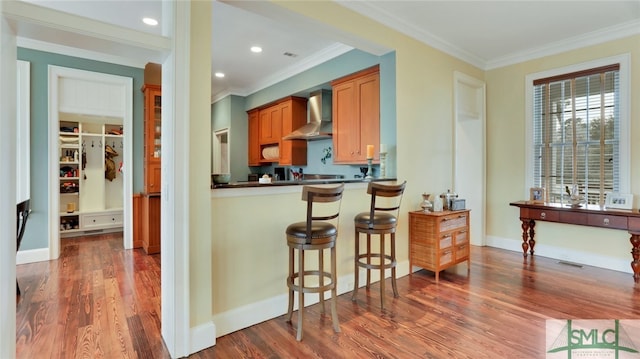 kitchen with a kitchen bar, wall chimney exhaust hood, crown molding, and dark hardwood / wood-style flooring